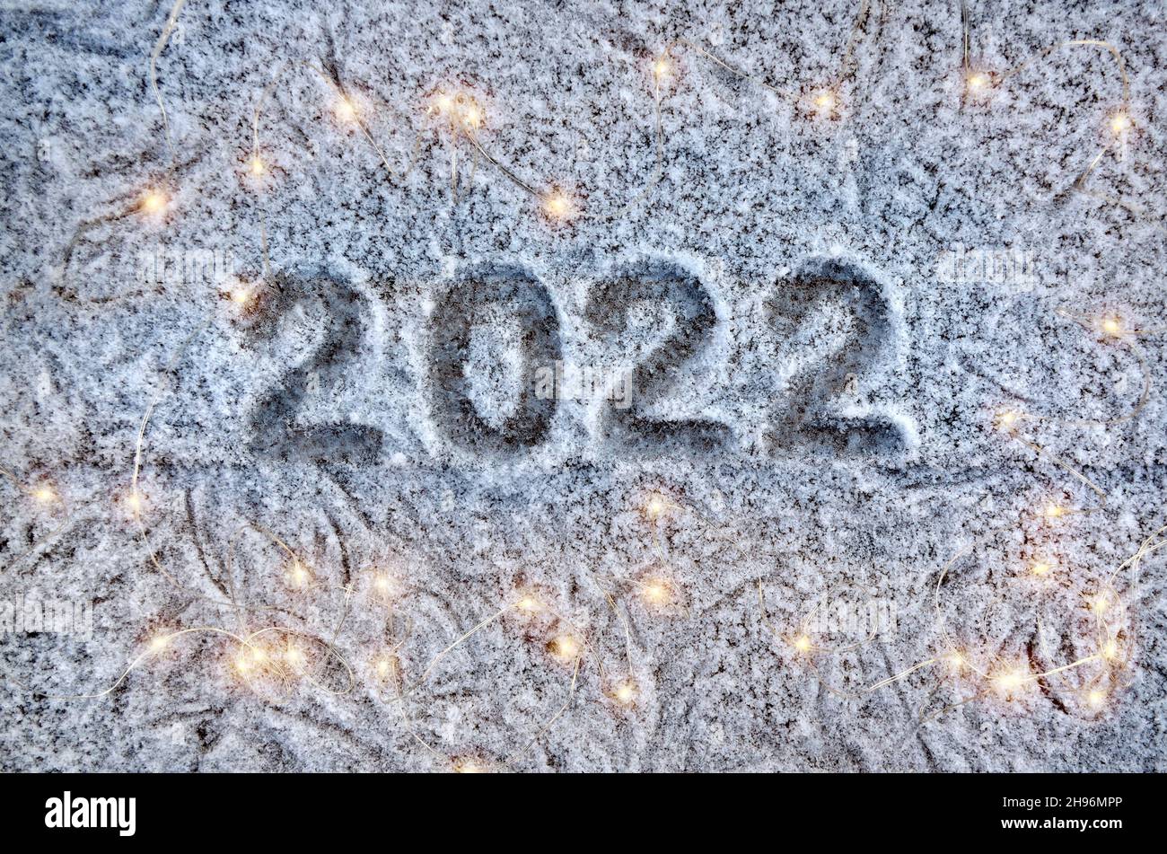 Inscription 2022 on a snow-covered surface with christmas lights. Happy new year 2022 concept. Stock Photo
