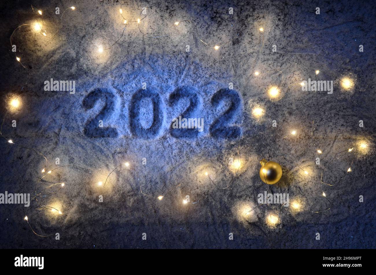 Inscription about the new year 2022 on the snow in winter with christmas lights. Happy New Year greetings concept. Stock Photo