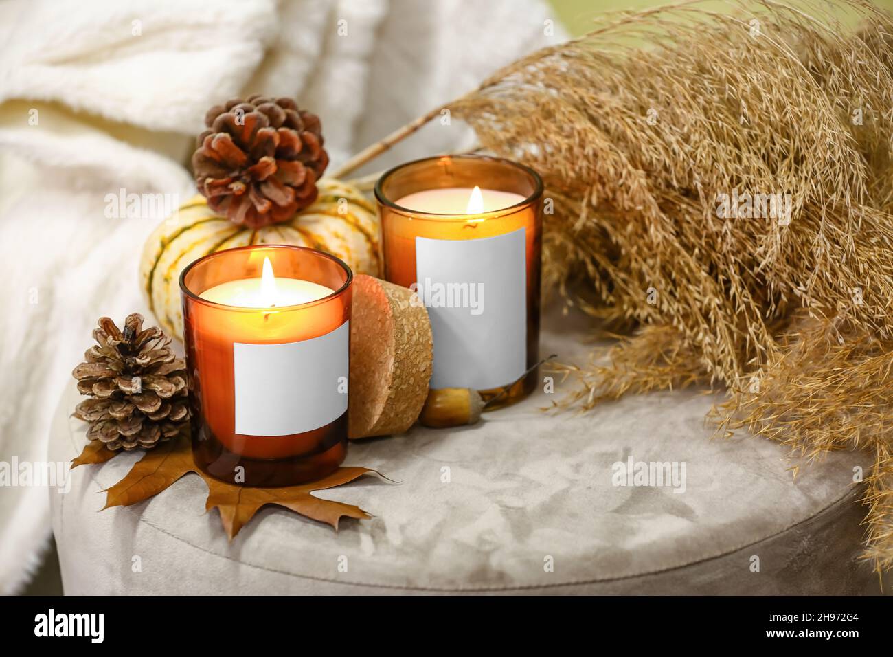 Burning candles in holders and autumn decor on pouf in room Stock Photo ...