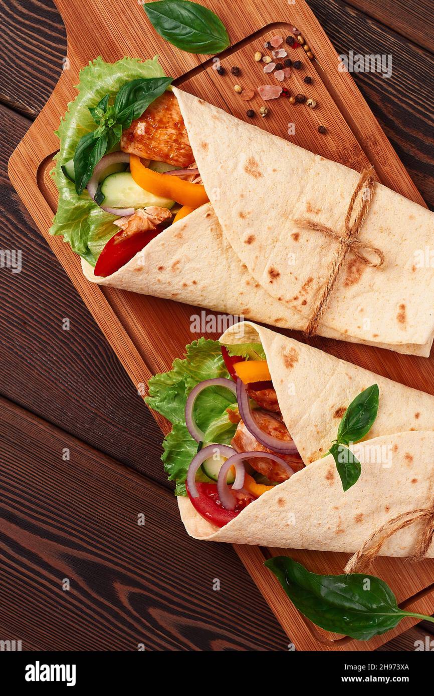 Tortilla wraps, grilled Mexican chicken with vegetables, burritos, on a wooden table, without people, Stock Photo