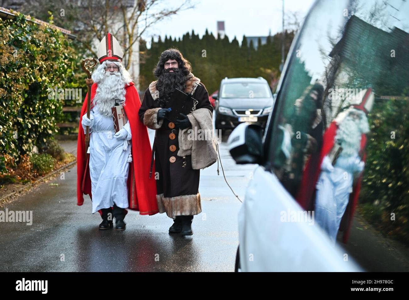 Friedrichshafen, Germany. 04th Dec, 2021. Dressed as St. Nicholas and his servant Ruprecht, Erich Schwarz (in red and with mitre) and Michael Huber (Ruprecht) come to the Herold family from Ailingen near Friedrichshafen. The two actors belong to the St. Nicholas Guild of Friedrichshafen, which wants to preserve the tradition of St. Nicholas of Myra. During the visit, the children of two families recite poems and musical pieces, and in return, St. Nicholas and Ruprecht read from their books, giving reprimands and praise. Credit: Felix Kästle/dpa/Alamy Live News Stock Photo