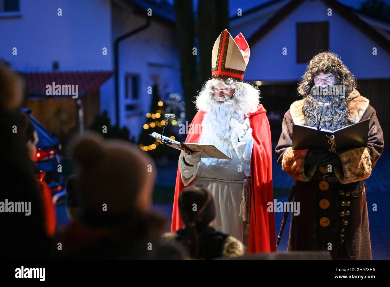 Friedrichshafen, Germany. 04th Dec, 2021. Dressed as St. Nicholas and his servant Ruprecht, Erich Schwarz (in red and with mitre) and Michael Huber (Ruprecht) visit the Herold family from Ailingen near Friedrichshafen. The two actors belong to the St. Nicholas Guild of Friedrichshafen, which wants to preserve the tradition of St. Nicholas of Myra. During the visit, the children of two families recite poems and musical pieces, and in return, St. Nicholas and Ruprecht read from their books, giving reprimands and praise. Credit: Felix Kästle/dpa/Alamy Live News Stock Photo