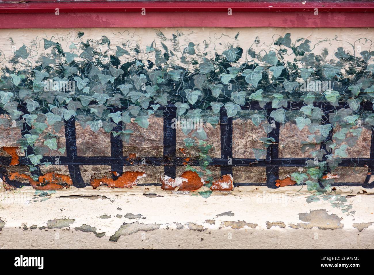 An exterior wall with a deteriorating mural depicting ivy growing on a fence.. Stock Photo