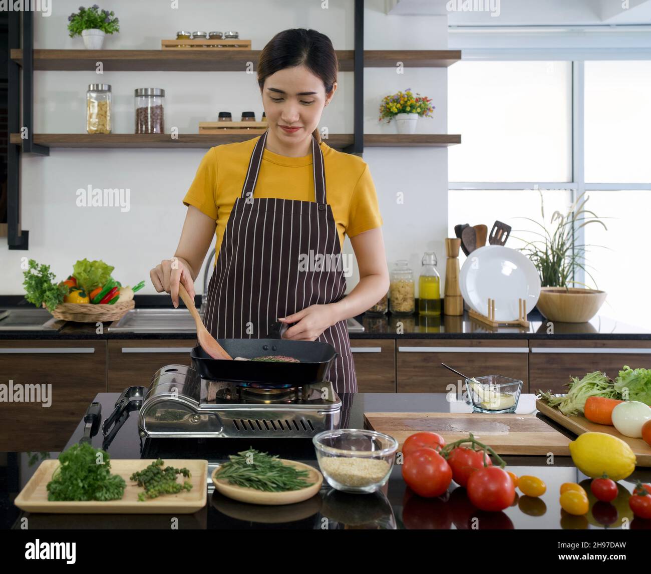 Young asian woman dressed in an apron cooking steak. The kitchen