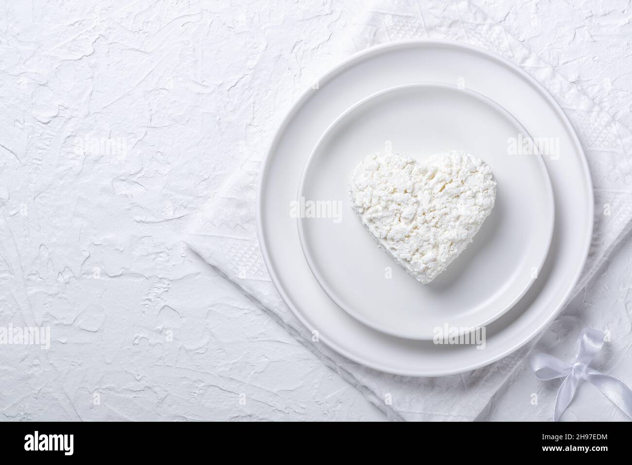 Heart shaped cottage cheese in a plate on a white table. Copy space for text Stock Photo