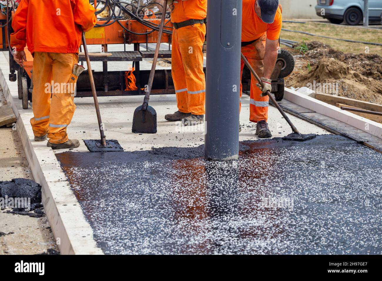 Road construction workers leveling hot asphalt, using a trowel tool to