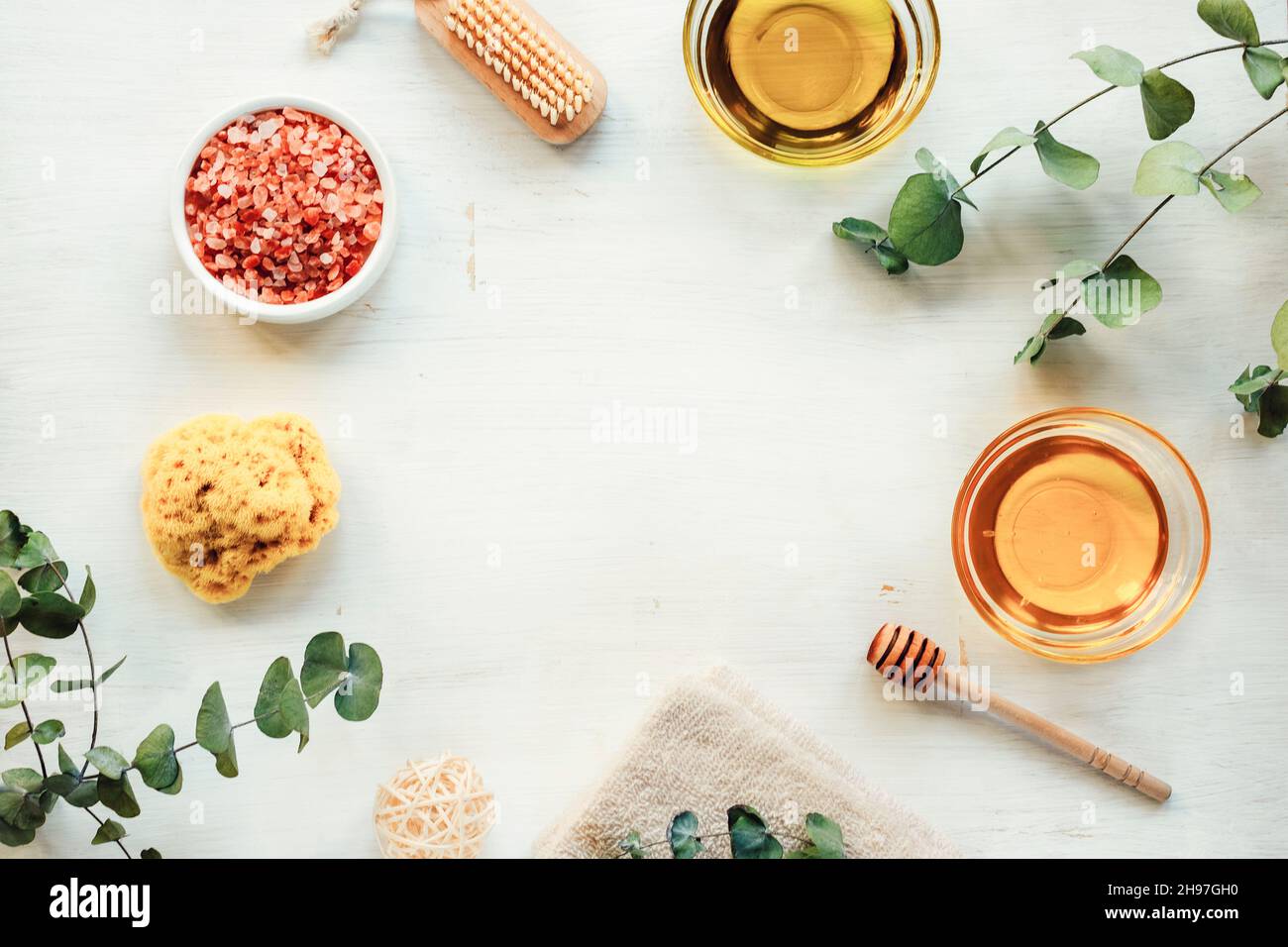 Natural ingredients for homemade scrub. Oil, honey, pink himalayan salt, face or body brush, sponge, towel and eucalyptus branches on white wooden Stock Photo