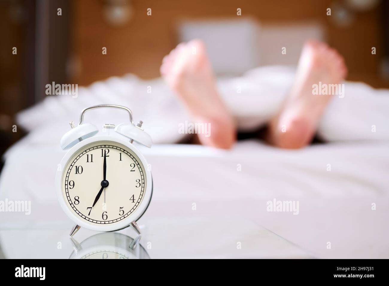 Sleeping woman legs in bed, early morning, alarm clock ringing. Selective focus. Laziness, lateness Stock Photo