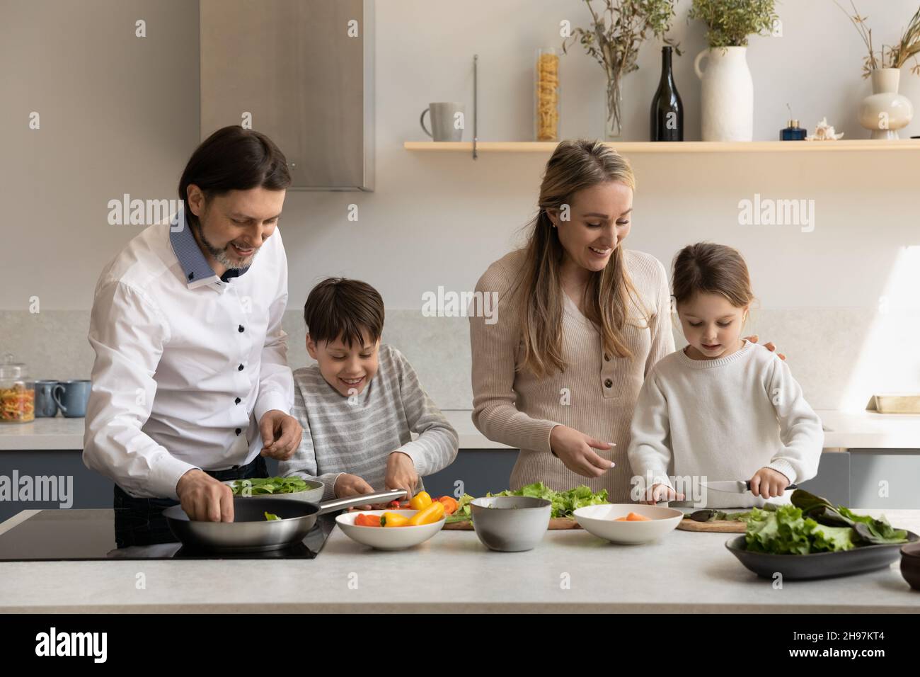 Happy parents cooking with small children at home. Stock Photo