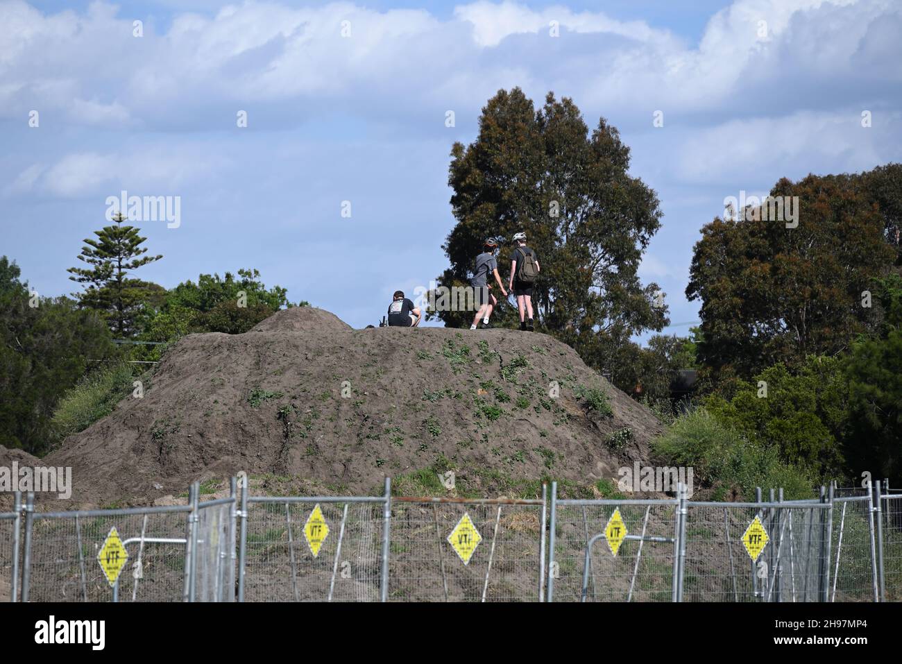 Three boys atop a mound of dirt, behind temporary fencing, at the wetland construction site in Elsternwick Park Nature Reserve Stock Photo