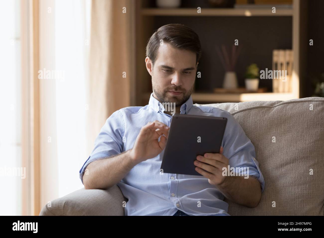 Serious freelance employee man using app on tablet at home Stock Photo