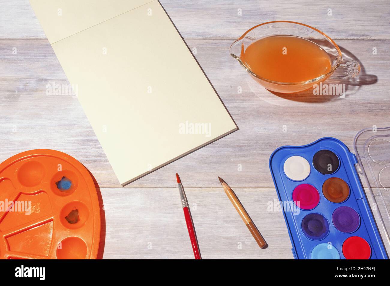 Watercolor painting. Sketchbook, watercolor paints, palette and cup of water on rustic table.  School concept. Free space for text or image Stock Photo