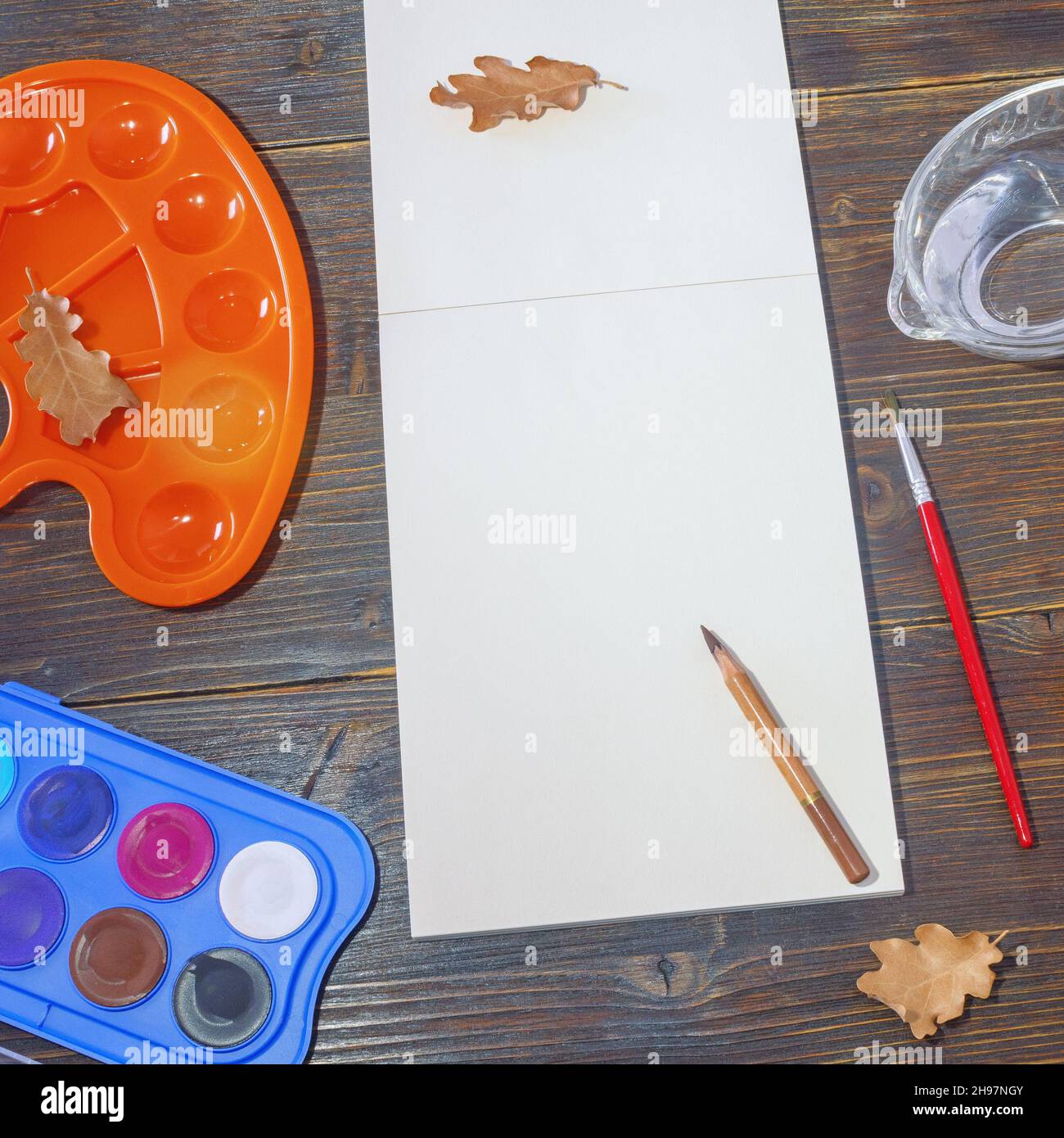 Sketchbook, watercolor paints, palette and dry autumn leaves on dark rustic table. School concept. Copy space Stock Photo