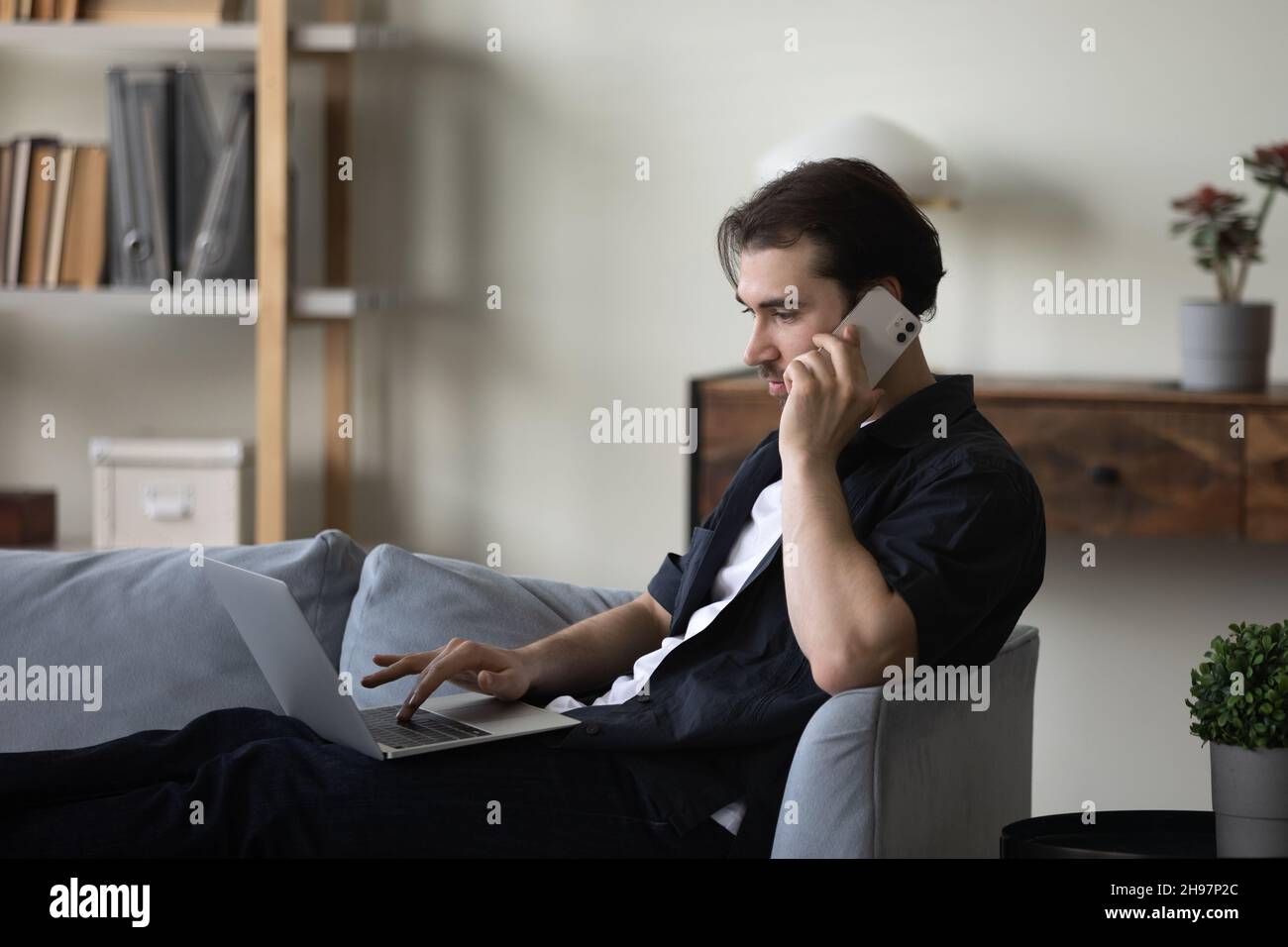 Serious busy freelance worker resting on couch, using laptop computer Stock Photo