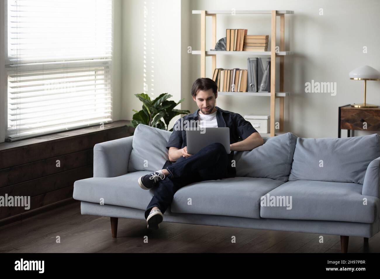Smiling man in casual using laptop computer on comfortable couch Stock Photo
