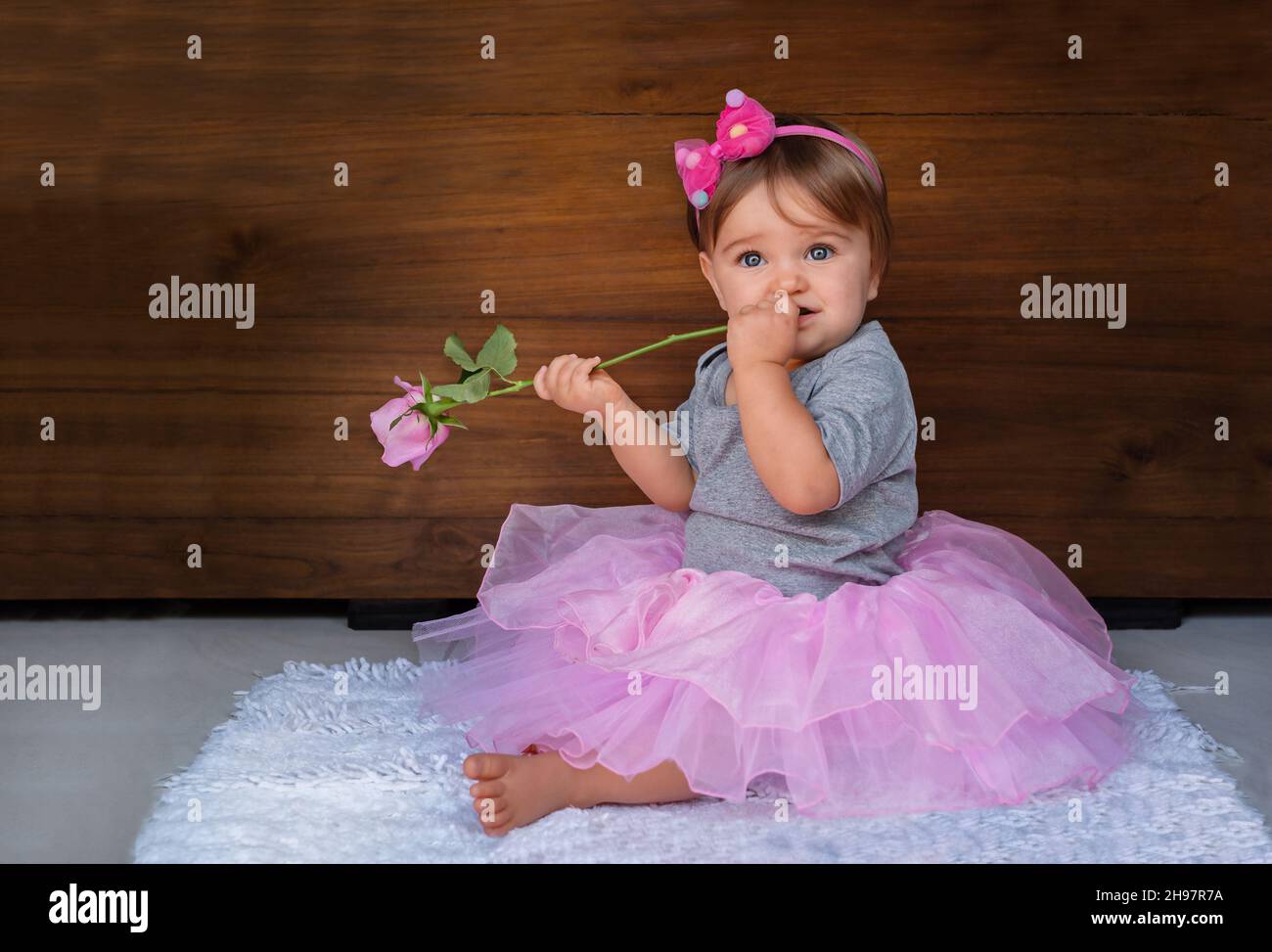 Portrait of a child with a rose on a wooden background. Baby girl in pink jewelry with a pink flower on a wood background. Stock Photo