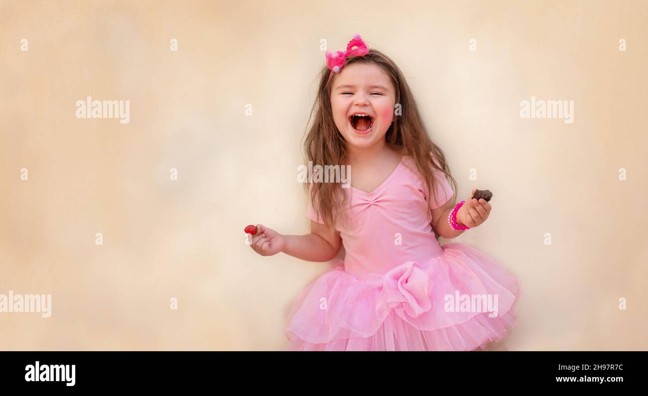 Child with strawberries and chocolate. Girl with red berries and chocolate in a pink dress on a yellow background Stock Photo