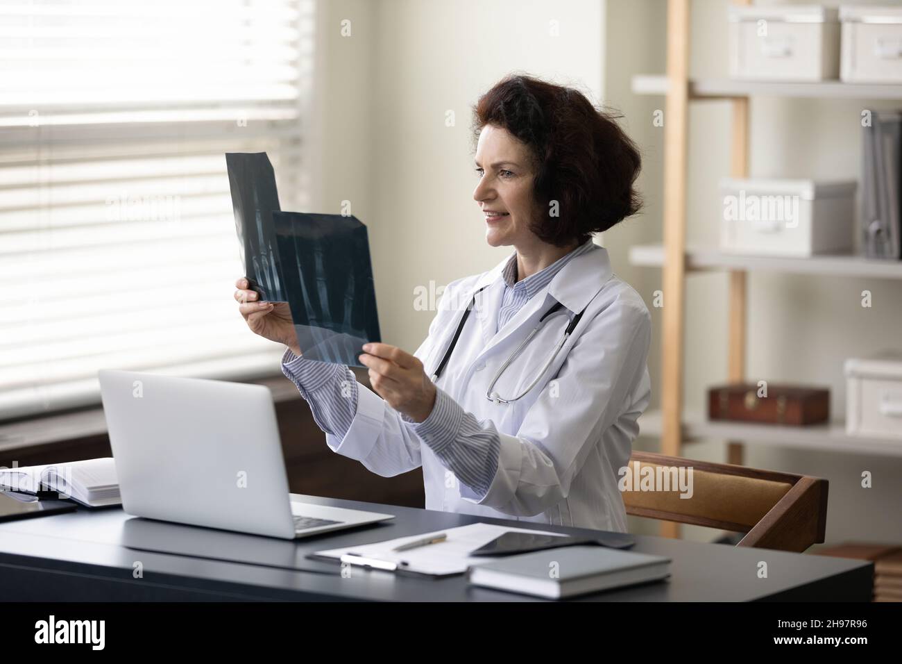 Smiling busy mature female doctor studying xray radiography images ...