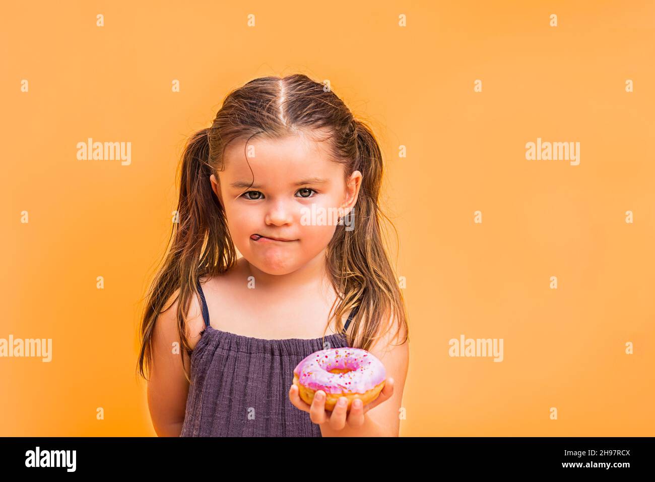 child girl holdind on the hand a pink donut.  on a yellow background Stock Photo
