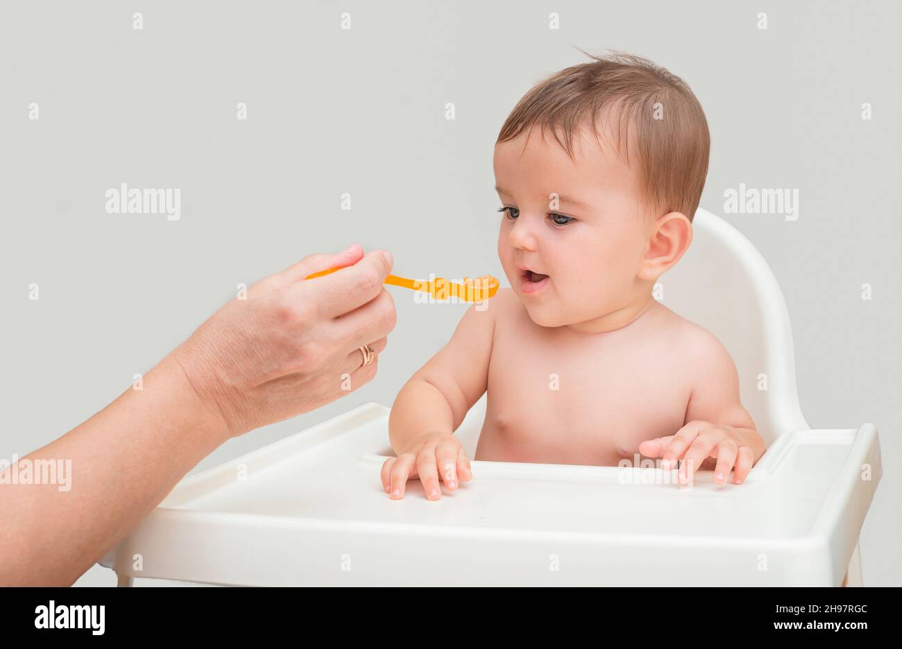 cute baby first meal.  mom's hand feeds the rabbi from a spoon with orange puree Stock Photo