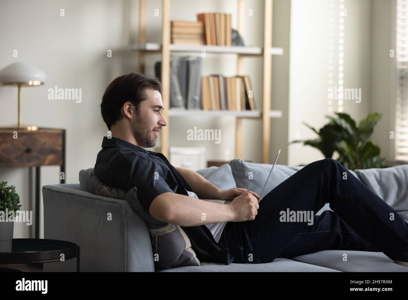 Happy smiling guy working at computer from home couch Stock Photo