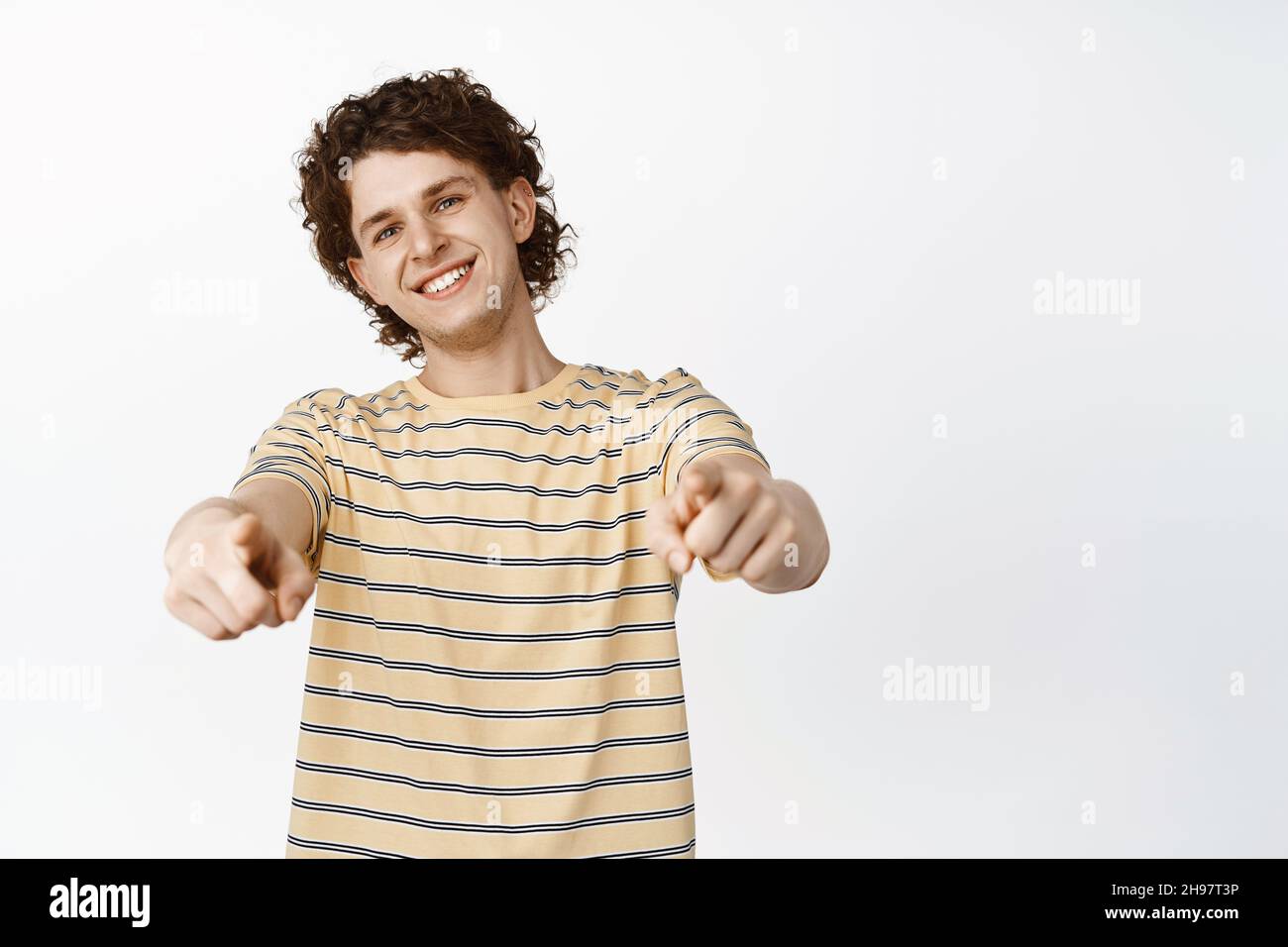 Smiling young man pointing fingers at camera with pleased and proud face, congratulating, picking you, standing over white background Stock Photo