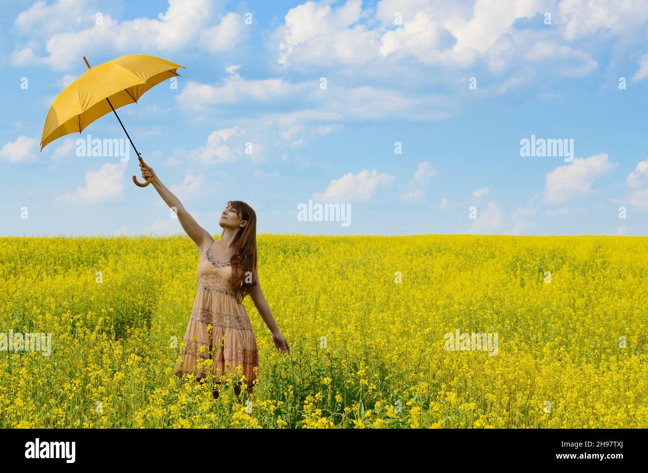 Young woman with umbrella at canola field Stock Photo