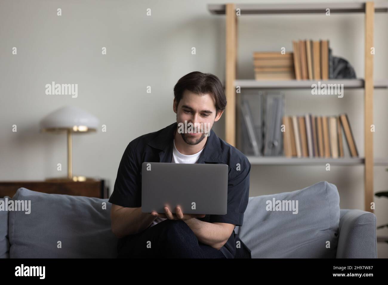 Happy smiling guy working at computer from home couch Stock Photo