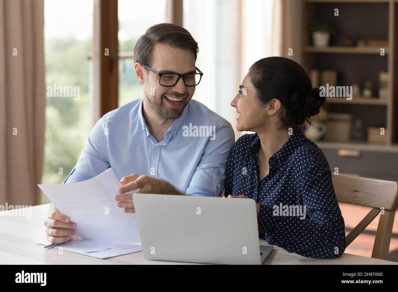 Happy multiethnic professional coworkers talking and laughing at workplace Stock Photo