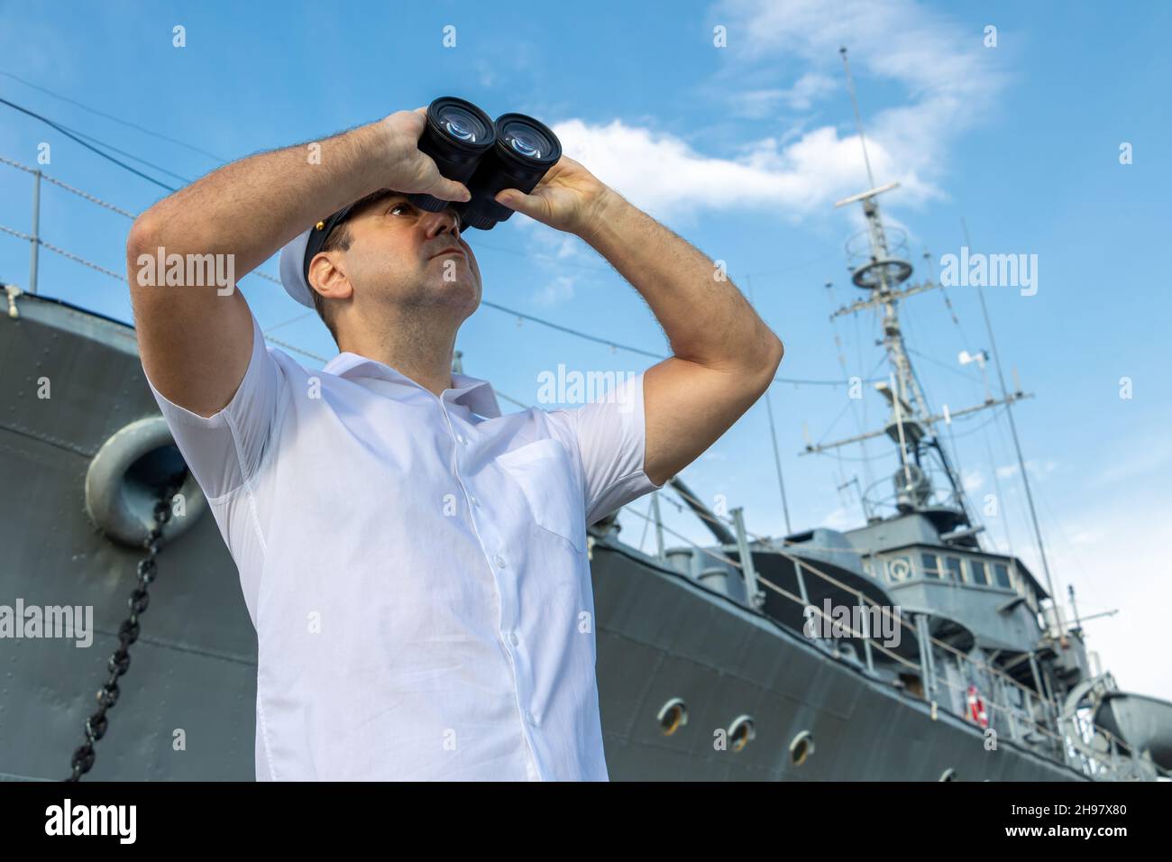 Navy officer standing beside warship and looking around with binocular. Stock Photo