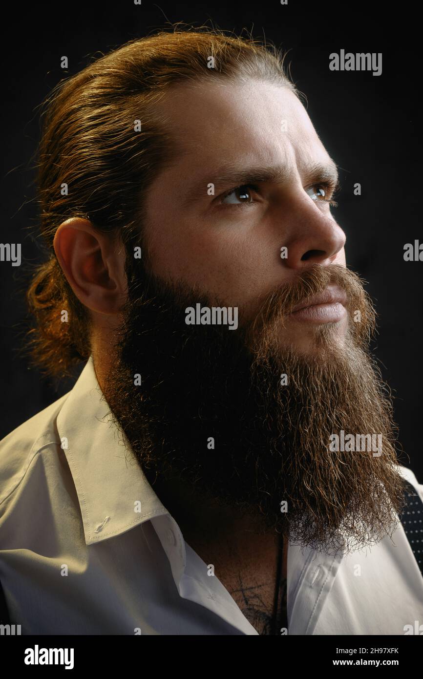 close-up portrait of a brutal man with a beard and long hair he looks up. Stock Photo