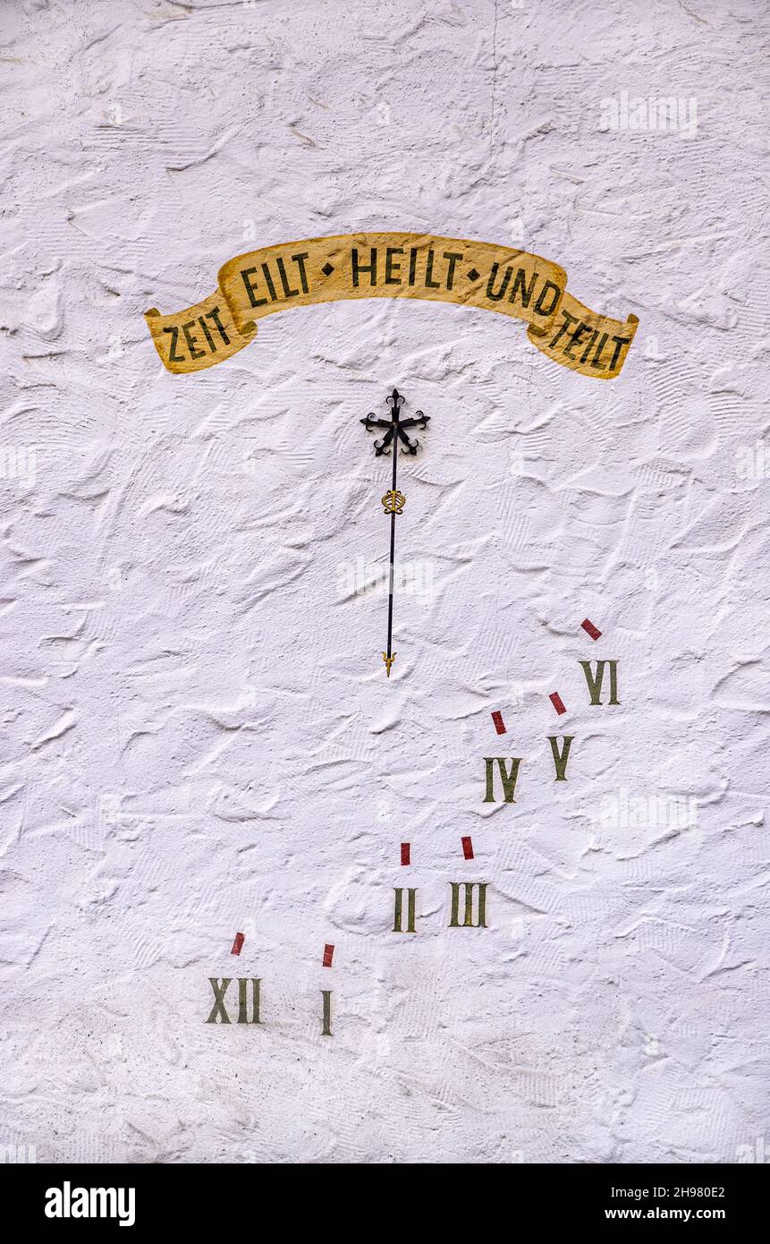 Sundial with motto in German ZEIT EILT HEILT UND TEILT (TIME RUNS HEALS AND DIVIDES) on a white house wall. Stock Photo