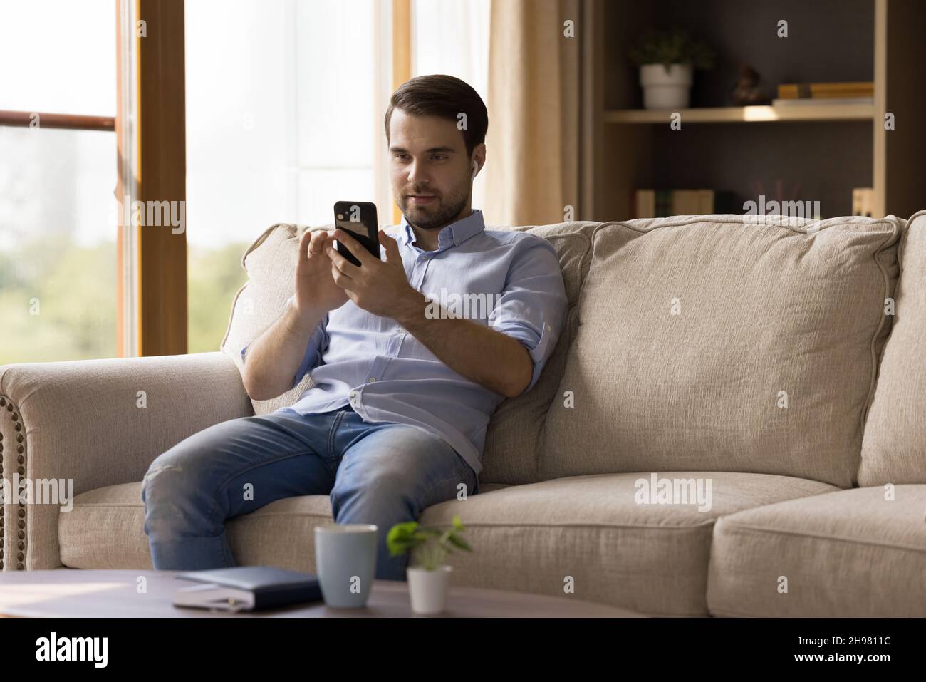 Millennial guy with earphones using media app on mobile phone Stock Photo