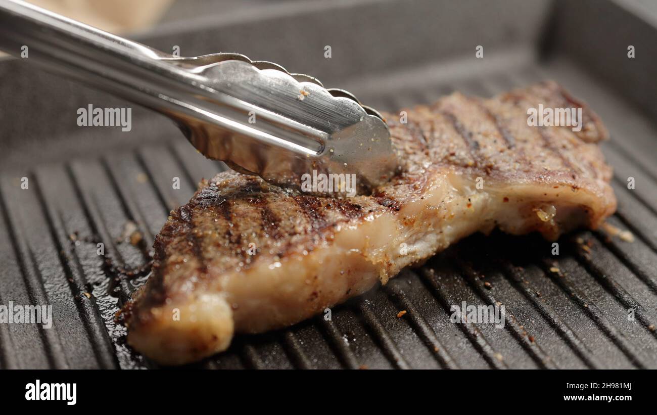 flip new york steak with tongs on grill pan, wide photo Stock Photo
