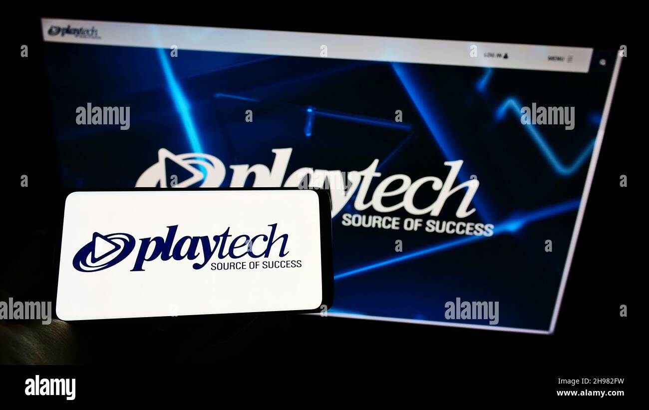 Person holding smartphone with logo of British gambling software company Playtech plc on screen in front of website. Focus on phone display. Stock Photo