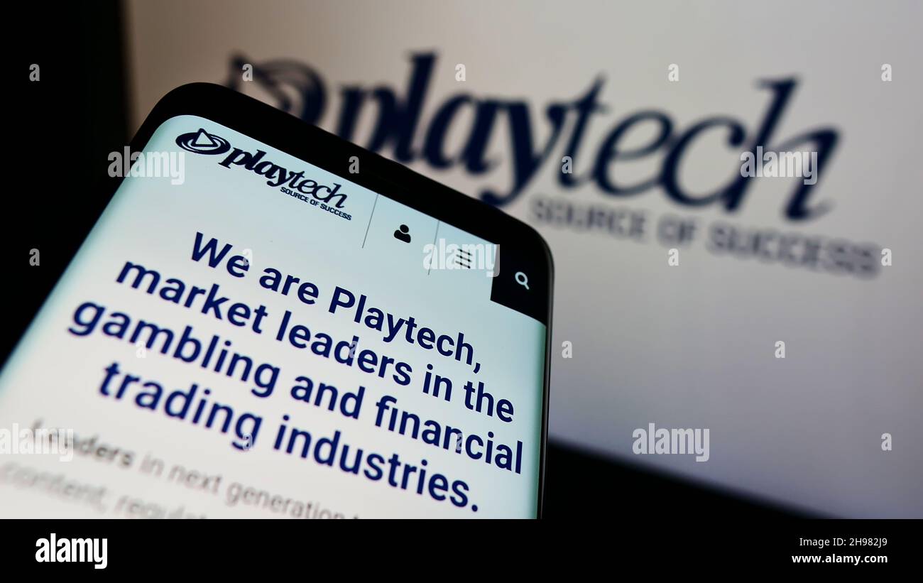 Mobile phone with website of British gambling software company Playtech plc on screen in front of business logo. Focus on top-left of phone display. Stock Photo