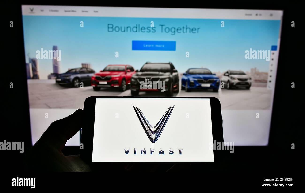 Person holding smartphone with logo of Vietnamese car manufacturer VinFast on screen in front of website. Focus on phone display. Stock Photo
