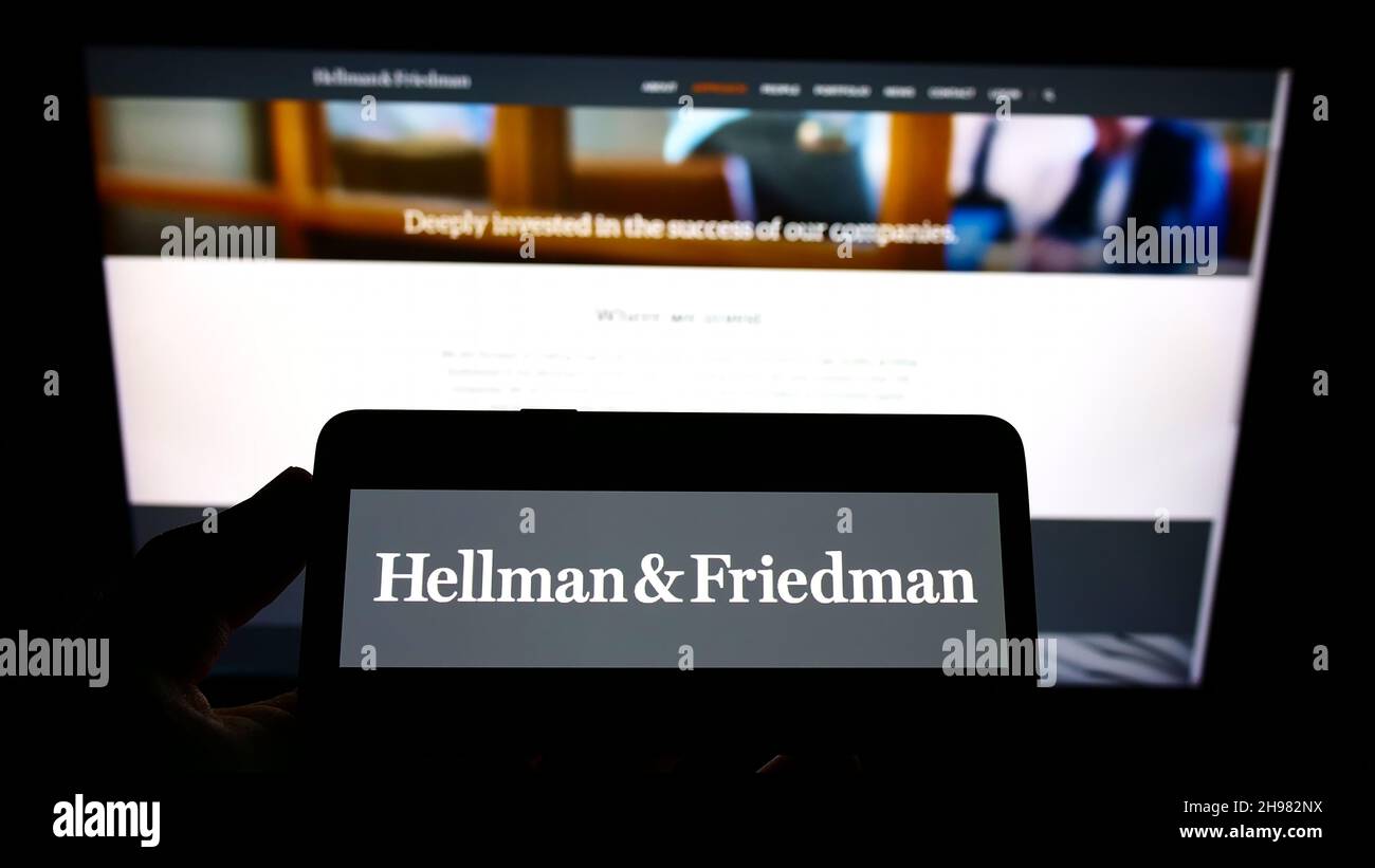 Person holding smartphone with logo of US private equity company Hellman and Friedman LLC on screen in front of website. Focus on phone display. Stock Photo
