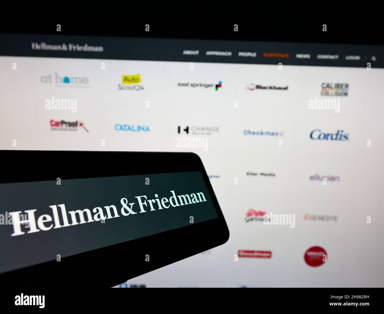 Cellphone with logo of US private equity company Hellman and Friedman LLC on screen in front of website. Focus on center-right of phone display. Stock Photo