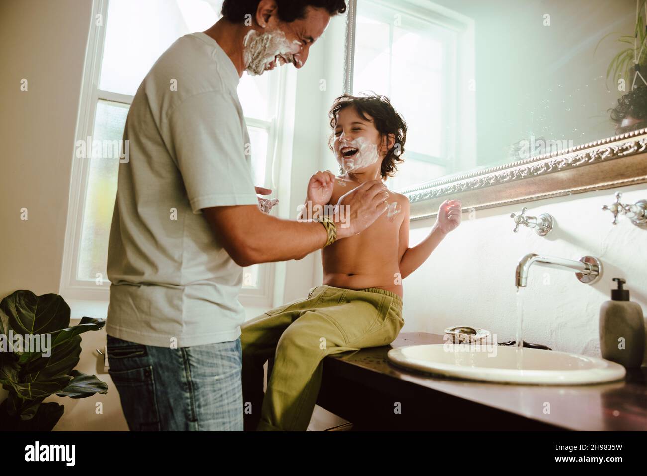 Playful father and son having fun with shaving foam in the bathroom. Father and son laughing cheerfully with shaving cream on their faces. Loving fath Stock Photo