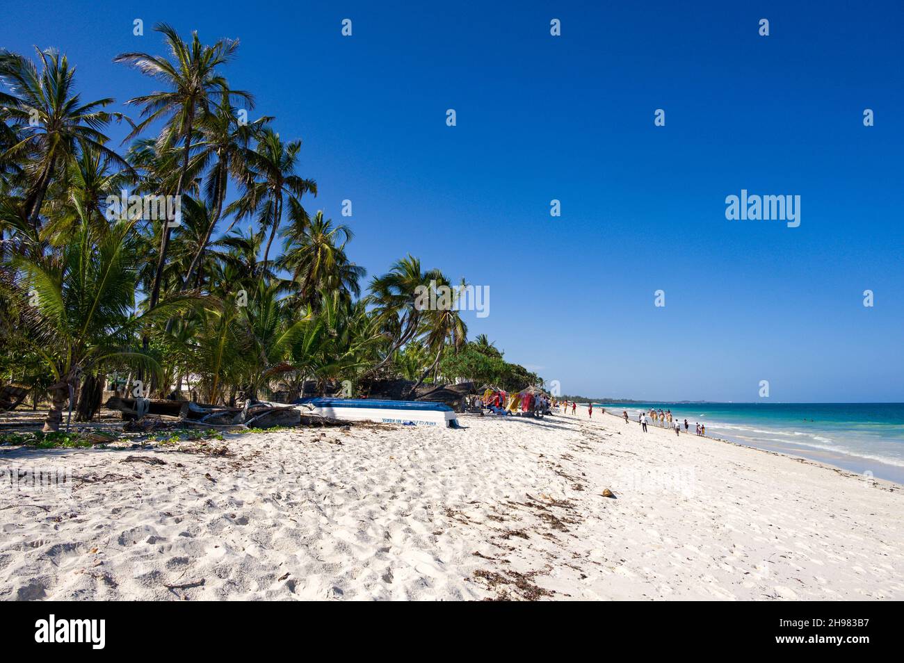 View along Diani beach lined by palm trees with tourists and locals walking on the beach, Kenya Stock Photo