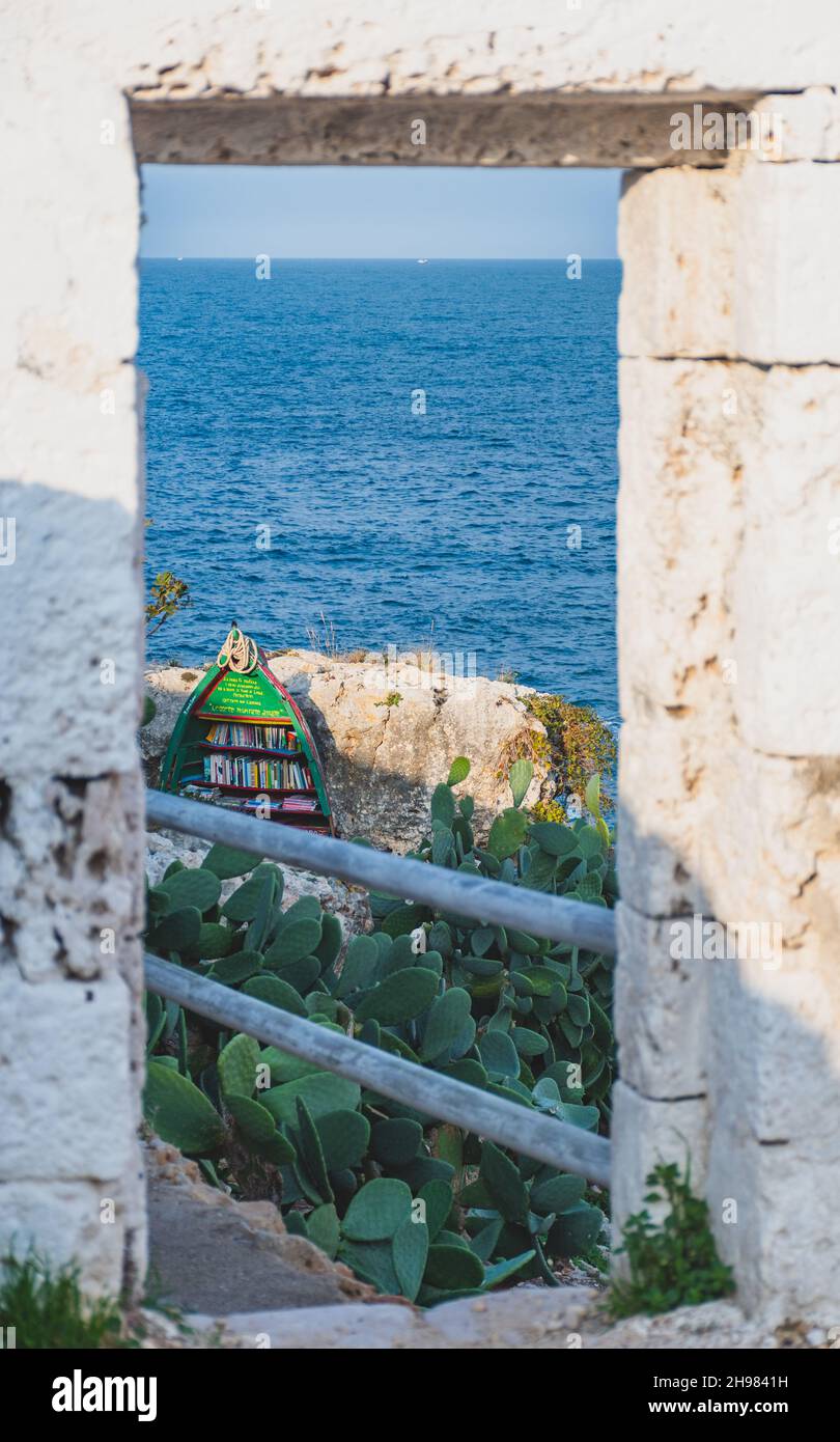 Mediterranean sea landscape with rocky cliff, beautiful blue sea, vegetation, stone walls and bookcase with shelves made in old boat Stock Photo
