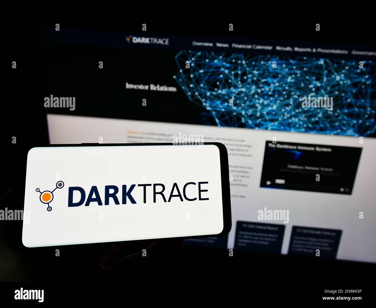 Person holding cellphone with logo of cyber defence company Darktrace plc on screen in front of business webpage. Focus on phone display. Stock Photo
