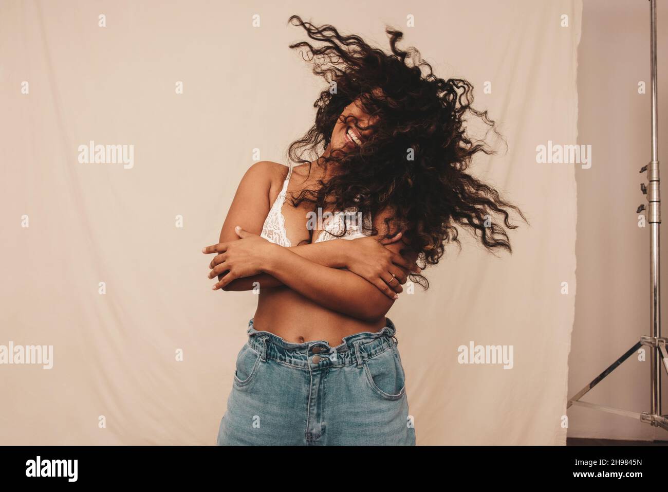 Woman whipping her hair in a studio. Happy young woman laughing cheerfully while standing against a studio background. Body positive young woman feeli Stock Photo