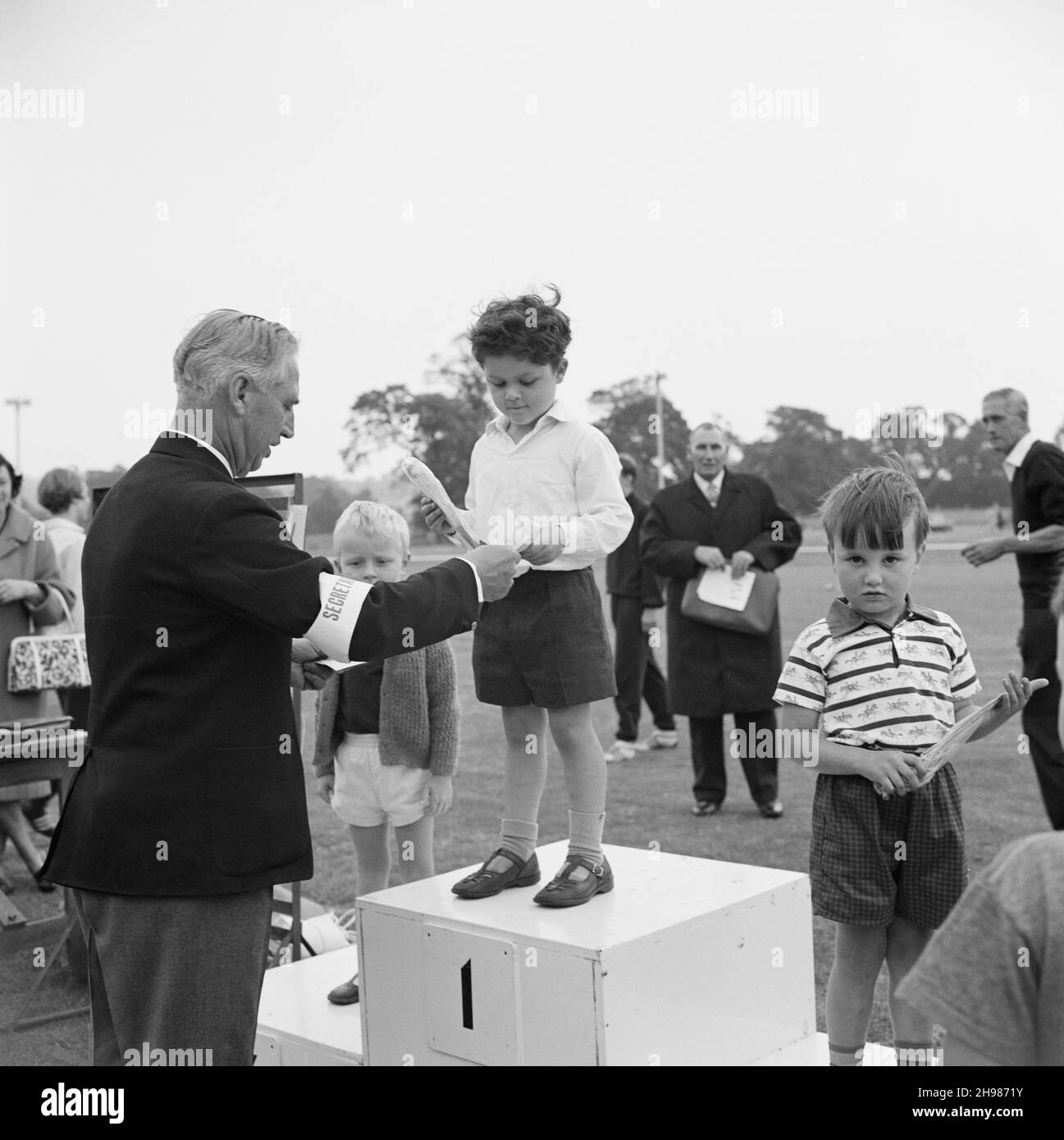 Copthall Stadium, Hendon, Barnet, London, 25/06/1966. A young boy on a podium being presented with a prize, at the annual Laing Sports Day held at Copthall Stadium. In 1966, the annual Laing employees' Sports Day was held on 25th June at Copthall Stadium in Hendon. It was the first time the event had been held there, having previously taken place the Laing Sports Ground at Elstree. A range of events included athletics and a football competition, and competitors travelled from the firm's regional offices and sites, including from Scotland and Carlisle. There was also a funfair, marching band, a Stock Photo