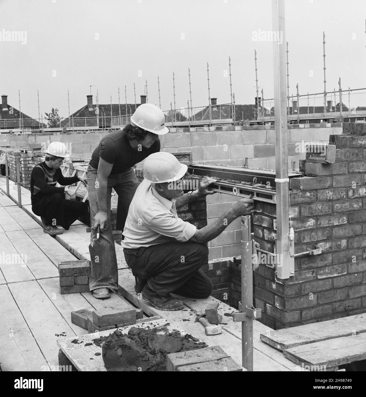 Furzehill Road, Borehamwood, Elstree and Borehamwood, Hertsmere, Hertfordshire, 20/09/1976. A man with a spirit level assessing the work of a Laing apprentice bricklayer during the construction of the Furzehill Road housing development. Laing began work on the Furzehill road contract in March 1976. 395 houses and flats would accommodate around 1,400 people. The site was a former 'Home of Rest for Horses,' giving rise to street names like Farriers Way. The contract became an unofficial training ground for apprentices and the old people's club on the development was built entirely by apprentices Stock Photo