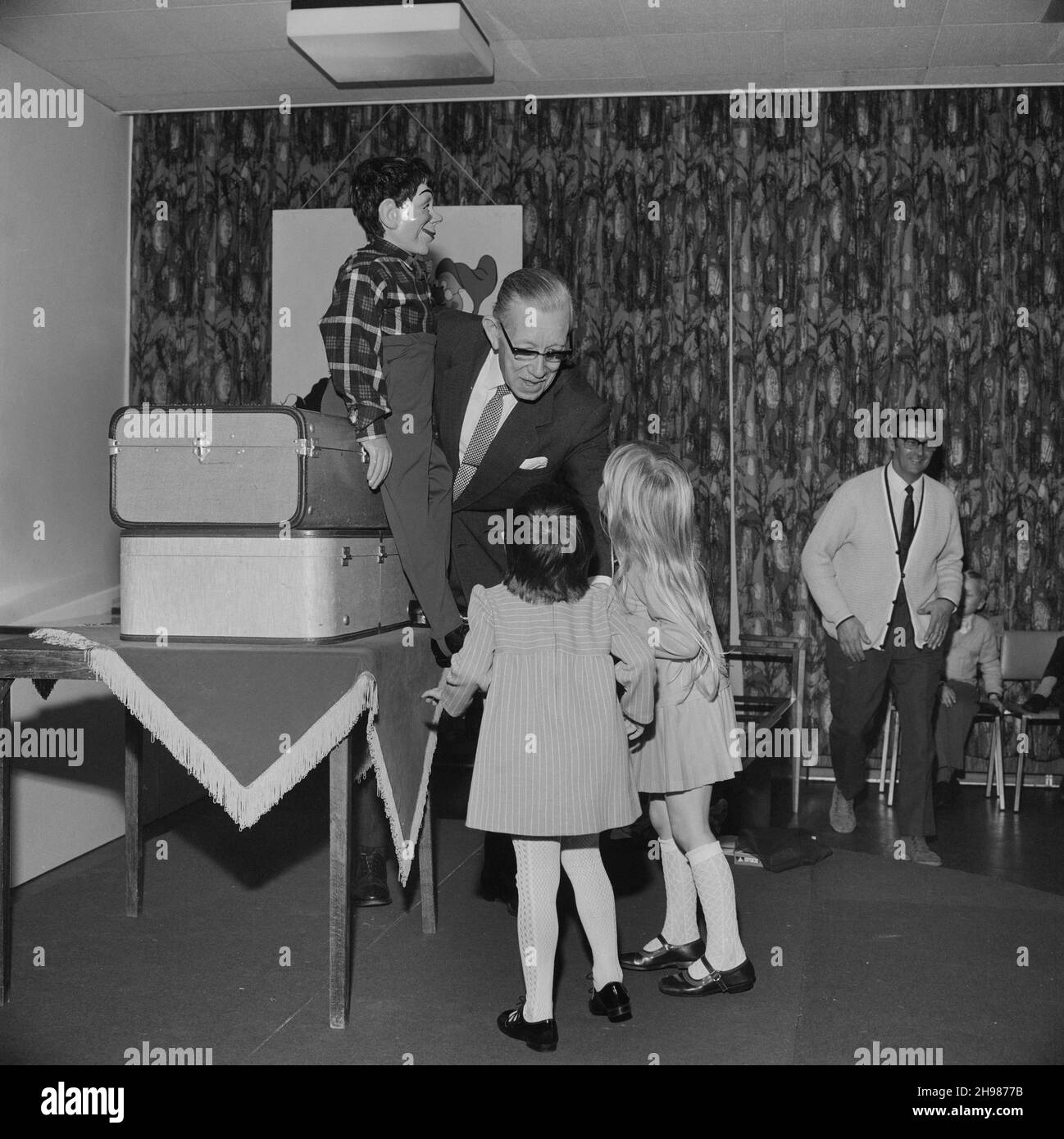 John Laing and Son Limited, Page Street, Mill Hill, Barnet, London, 15/12/1973. An entertainer with a ventriloquist's dummy speaking to two young girls at the annual children's Christmas party held by the Laing Sports Club at John Laing and Son Ltd's Mill Hill offices. The Laing Sports Club held its annual children's Christmas party on Saturday 15th December. The party was for 120 children aged under 7 years; older children saw a pantomime of Cinderella at Wembley. The children's party at the Mill Hill offices featured games, a traditional tea and a cartoon show, followed by a visit from Fathe Stock Photo
