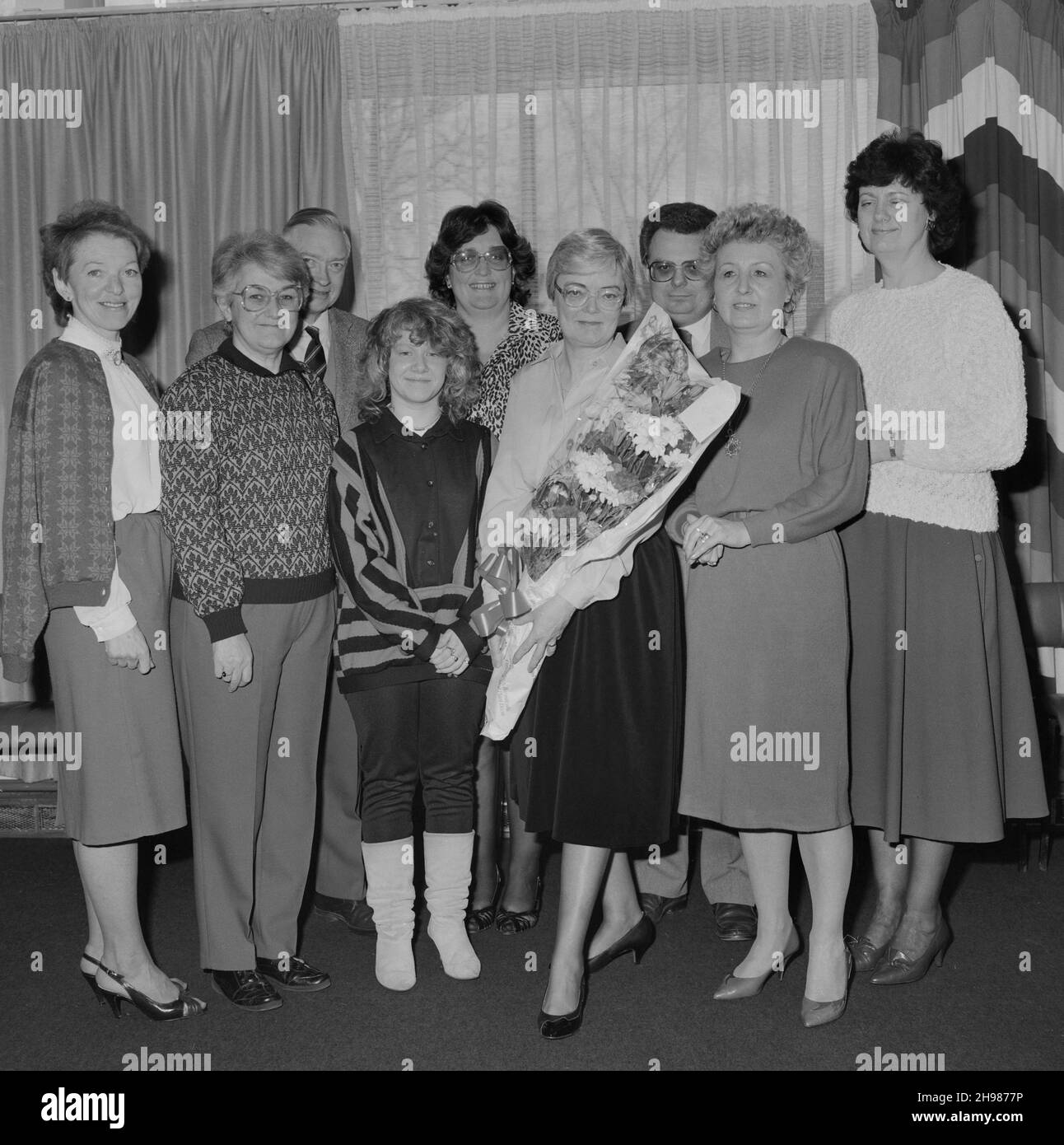 John Laing and Son Limited, Page Street, Mill Hill, Barnet, London, 30/03/1987. Mrs Joan Kirby posed holding a bouquet with a group of friends and colleagues during her retirement presentation at Mill Hill. Joan Kirby joined Laing in 1955 as a secretary for Mr Waldrum, who was in charge of personnel. She went on to work for various other individuals including John Renshaw. Joan joined Laing's Welfare Department in 1982 and retired from the Company in 1987, after 32 years of service. Stock Photo