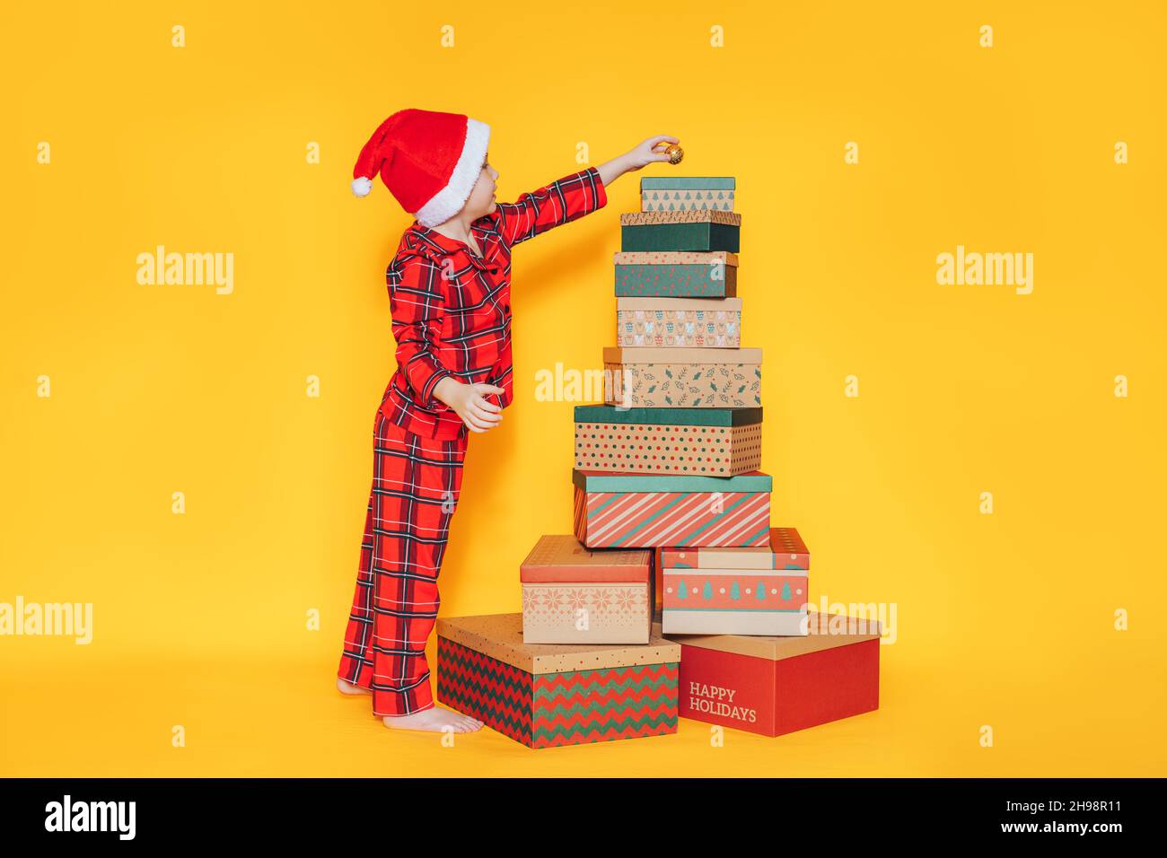 Bauble Stack Boy putting bauble on stack of christmas gifts against yellow ...