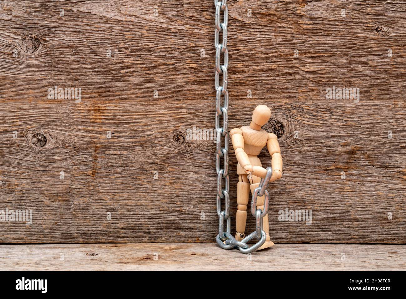 Wooden mannequin with a metal chain on wooden background. Get freedom. Stock Photo